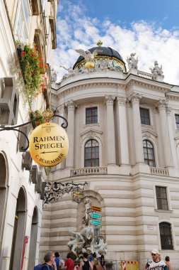 Viyana, Avusturya. Michaelerplatz 'daki eski bir el işi dükkanının işareti. Arka planda Habsburg Sarayı kompleksinin barok iç kısımları olan tarihi bir binasının kubbesi var. Dikey görüntü. 2023-08-02.