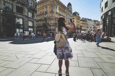 Viyana, Avusturya. Stock-im-Eisen-Platz ve Graben caddesinin manzarası. Arkadan genç bir bayan turist görülüyor. Telefonuyla fotoğraf çekmeye çalışıyor. 2023-08-02.