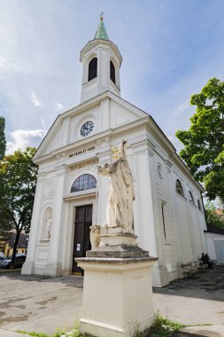 Viyana, Avusturya. St. Oswald Kilisesi, Altmannsdorf Katolik Kilisesi ön planda Khleslplatz 'daki Aziz Augustine heykeli. Dikey görüntü. 2023-08-02.