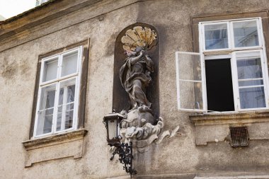 Viyana, Avusturya. Şehrin tarihi merkezinde, Griechengasse Caddesi 'ndeki antik bir binanın ön cephesinde, iki pencere arasında adak heykeli ve eski sokak lambası. 2023-08-02.