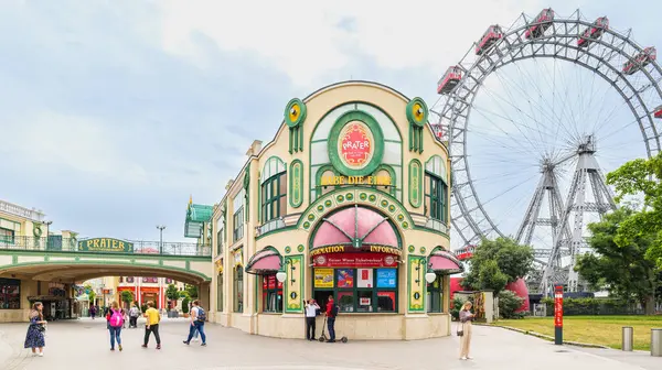 Viyana, Avusturya. Prater Lunaparkı 'nın bilet bürosu binası. Klasik ve sanat eseri tabelası ve süslemeleri var. İnsanlar giriyor. Arka planda dönme dolap beliriyor. 2023-08-04.