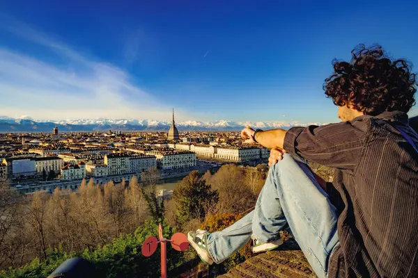トリノ イタリア カプチーニャヒルから 壁に座っている少年が景色を眺め 指で市内中心部を指差します モール アントネッリアナと雪に覆われたアルプス 2024 ストック画像