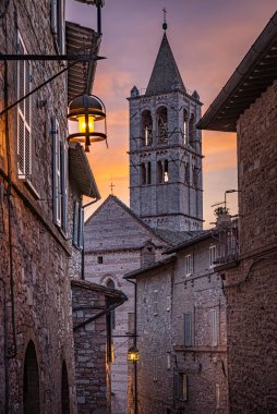 Assisi, İtalya. Gün batımında Via Sermei 'nin eski binalarından Santa Chiara Bazilikası' nın manzarası. Tarihi merkezde eski ortaçağ evleri olan dar bir sokak. Dikey resim. 