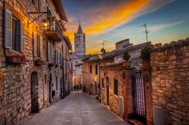 Assisi, İtalya. Gün batımında Via Sermei 'den Santa Chiara Bazilikası manzarası. Orta Çağ 'ın tarihi merkezinde eski evleri olan dar bir sokak.. 