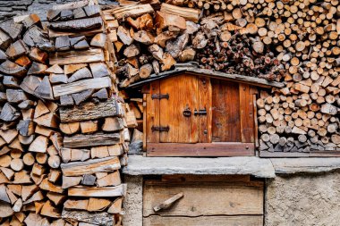 Pontechianle, Italy. Wooden logs stacked on the wall of a mountain house. Miniature wooden house for storing tools. clipart