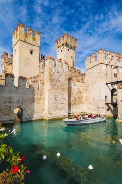 Sirmione, İtalya. Kale rıhtımında bir tekne ile Scaligero Kalesi 'nin manzarası. Aktivite ve seyahat deneyimi. Kale hendeği. Eğlence tekneleri için seyir kanalı. 2024-09-22.