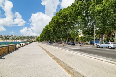 Napoli, İtalya. Francesco Caracciolo 'yu boşaltın. Geniş gezinti alanı, ağaçlarla kaplı bulvarı, körfez üzerinde az sayıda arabası ve mavi gökyüzü olan deniz önü; yaz kıyı şeridi manzaralı. 2025-07-28.