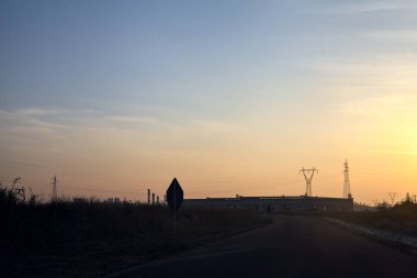 Gün batımında terk edilmiş depoları ve sütunları olan boş bir yol