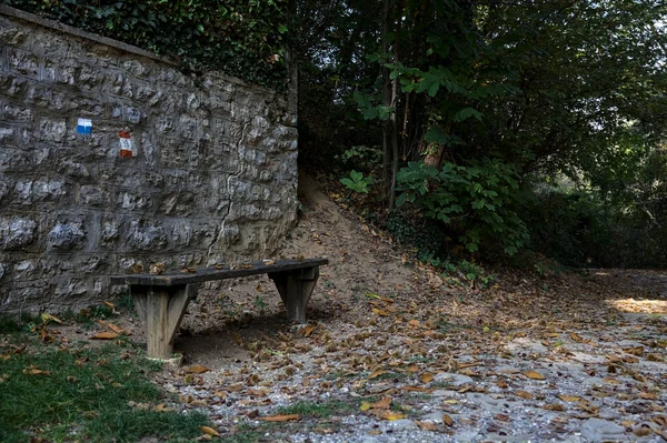 森林里的一条肮脏的路 边上有一堵石墙和一条长椅 — 图库照片