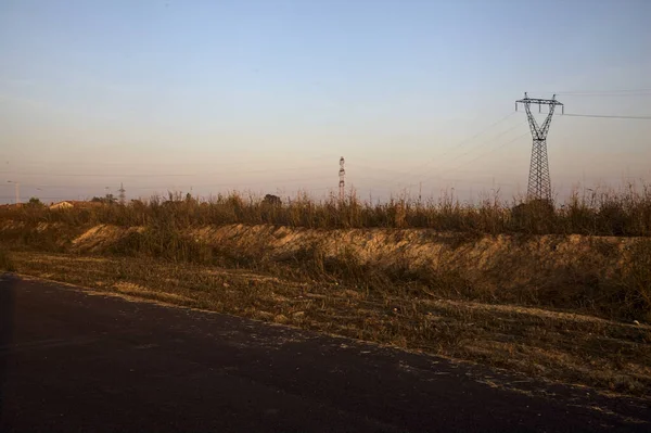 stock image Electricity pylon in a field behind an embankment at the edge of a country road at sunset