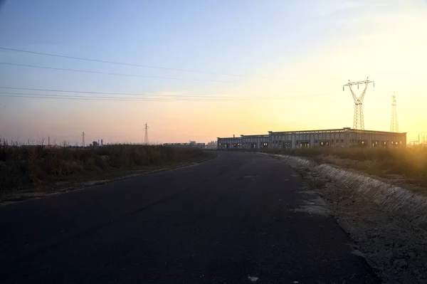 stock image Empty road with abandoned warehouses and pylons at sunset