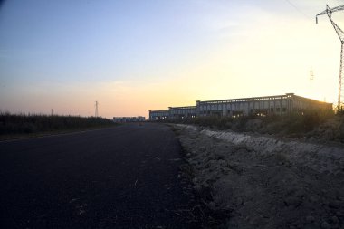 Gün batımında terk edilmiş depoları ve sütunları olan boş bir yol