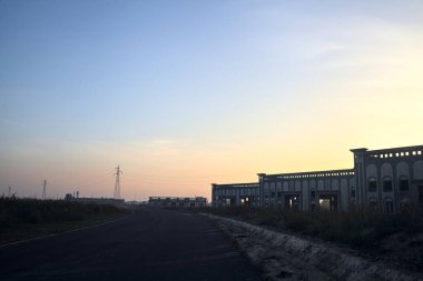 Gün batımında terk edilmiş depoları ve sütunları olan boş bir yol