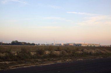 Uzaklarda terk edilmiş bir malikanesi ve deposu olan bir endüstriyel tesiste çıplak bir arazi.