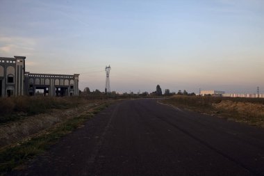 Gün batımında terk edilmiş depoları ve sütunları olan boş bir yol