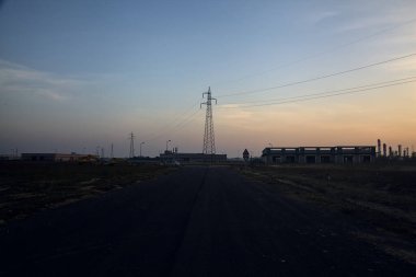 Terk edilmiş depo ve sütunlar gün batımında bir sanayi tesisinde kavşağın yanında.