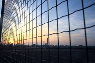 Gün batımında çıplak bir arazinin ötesinde, ufukta sanayi tesisi görünüyor.