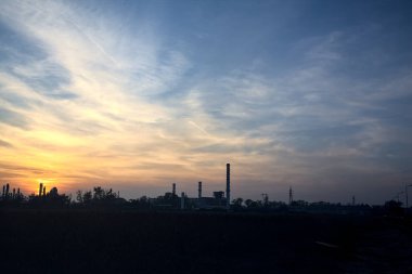 Gün batımında çıplak bir arazinin ötesinde, ufukta sanayi tesisi görünüyor.