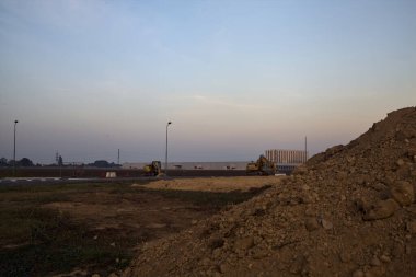 Gün batımında endüstriyel bir tesiste döner kavşağın kenarında kazıcılar.