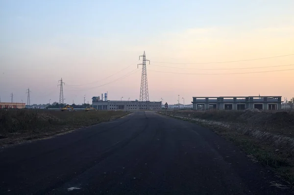 Abandoned warehouses and pylons next to a roundabout in an industrial complex at sunset