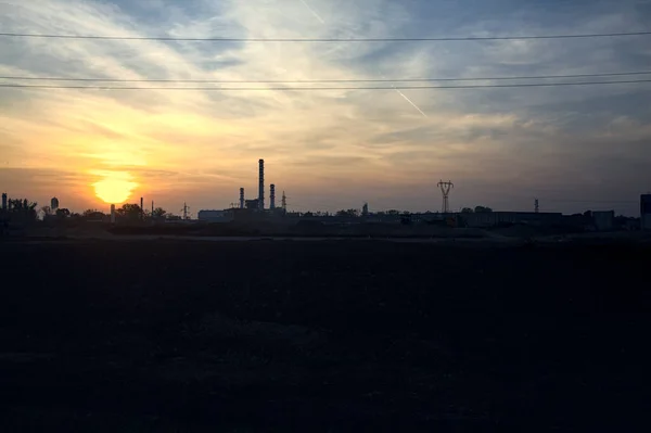 stock image Industrial complex on the horizon beyond a bare field at sunset