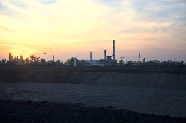 stock image Industrial complex on the horizon beyond a bare field at sunset