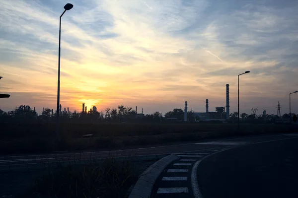 Abandoned warehouse in a field with an industrial complex in the distance at sunset