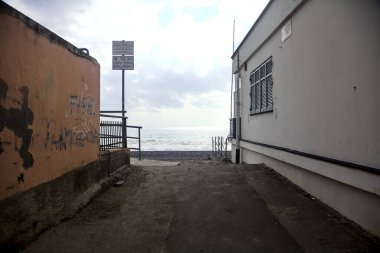 Bulutlu bir günde iki alçak bina tarafından çerçevelenmiş deniz kıyısındaki bir sahile erişim