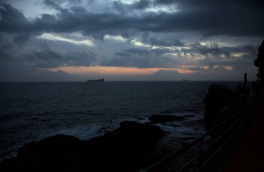Bulutlu bir günde deniz alacakaranlıkta ufukta bir yük gemisiyle