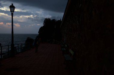 Alacakaranlıkta deniz kenarındaki bir uçurumda sokak ışıklarıyla panoramik yürüyüş