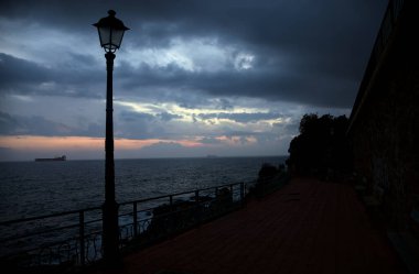 Alacakaranlıkta deniz kenarındaki bir uçurumda sokak ışıklarıyla panoramik yürüyüş