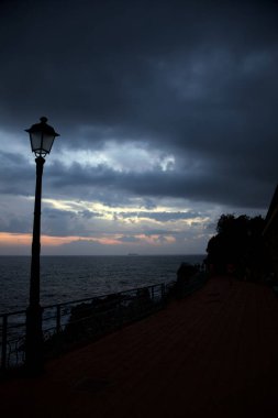 Alacakaranlıkta deniz kenarındaki bir uçurumda sokak ışıklarıyla panoramik yürüyüş
