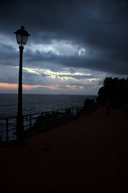 Alacakaranlıkta deniz kenarındaki bir uçurumda sokak ışıklarıyla panoramik yürüyüş