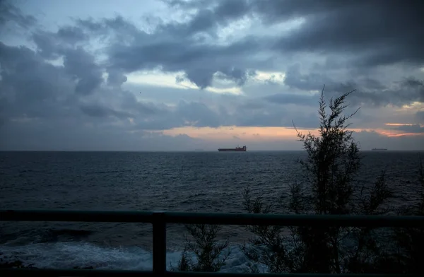 stock image Sea on cloudy day at dusk with a cargo ship in the distance framed by a railing