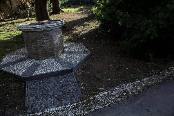 stock image Old brick well next to a bush in a park