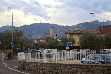 Malcesine 'deki Scaligero şatosunun kulesi ağaçlar ve zakkum bitkileriyle çevrili ve arka planda bir dağ sırtı var.