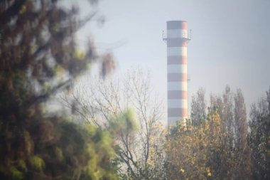 Sonbaharda sisli bir günde ağaçlar tarafından çerçevelenmiş kırmızı ve beyaz baca.