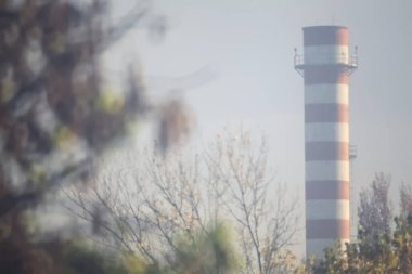 Sonbaharda sisli bir günde ağaçlar tarafından çerçevelenmiş kırmızı ve beyaz baca.