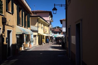 Dükkanlarla dolu dar bir cadde ve eski bir köyden geçen insanlar.