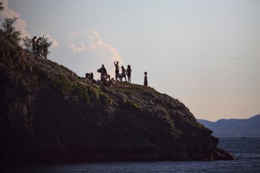 Gölün kıyısındaki bir kayada yaşayan gençler uzaktan görülmeye çalışılıyor.