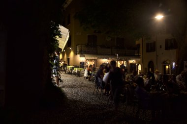 Restoranı olan bir meydan ve geceleri yemek yiyen insanlar.