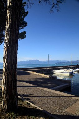 Güneşli bir günde, bir gölün üzerinde uzanan bir rıhtımın demirlemesi ve uzak bir dağ sırtı.