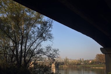 Sonbaharın açık bir gününde köprünün çerçevelediği uzaklıktaki demiryolu köprüsü