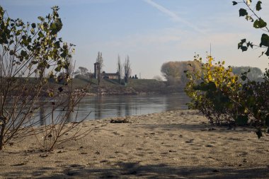 İtalya 'nın kırsal kesimindeki bitki ve çalıların çerçevelediği bir barajın arkasındaki nehir kenarındaki çan kulesi.