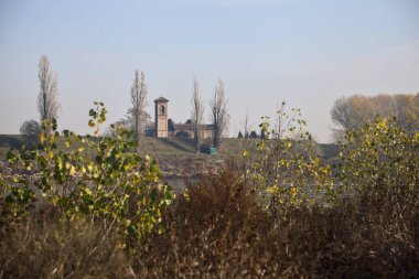 İtalya 'nın kırsal kesimindeki bitki ve çalıların çerçevelediği bir barajın arkasındaki nehir kenarındaki çan kulesi.