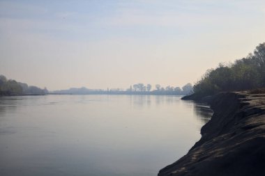 Sonbaharda kumlu bir sahilde, ağaçların yansıdığı nehir sulardan görülebiliyor.