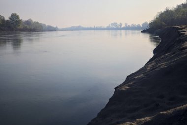 Sonbaharda kumlu bir sahilde, ağaçların yansıdığı nehir sulardan görülebiliyor.