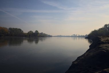 Sonbaharda kumlu bir sahilde, ağaçların yansıdığı nehir sulardan görülebiliyor.