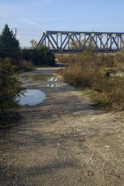 Kırsal kesimde arka planda köprüsü olan çamurlu bir yol.