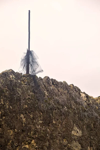 Net stuck in a metallic pole on the top of a stone wall with a cloudy sky as background